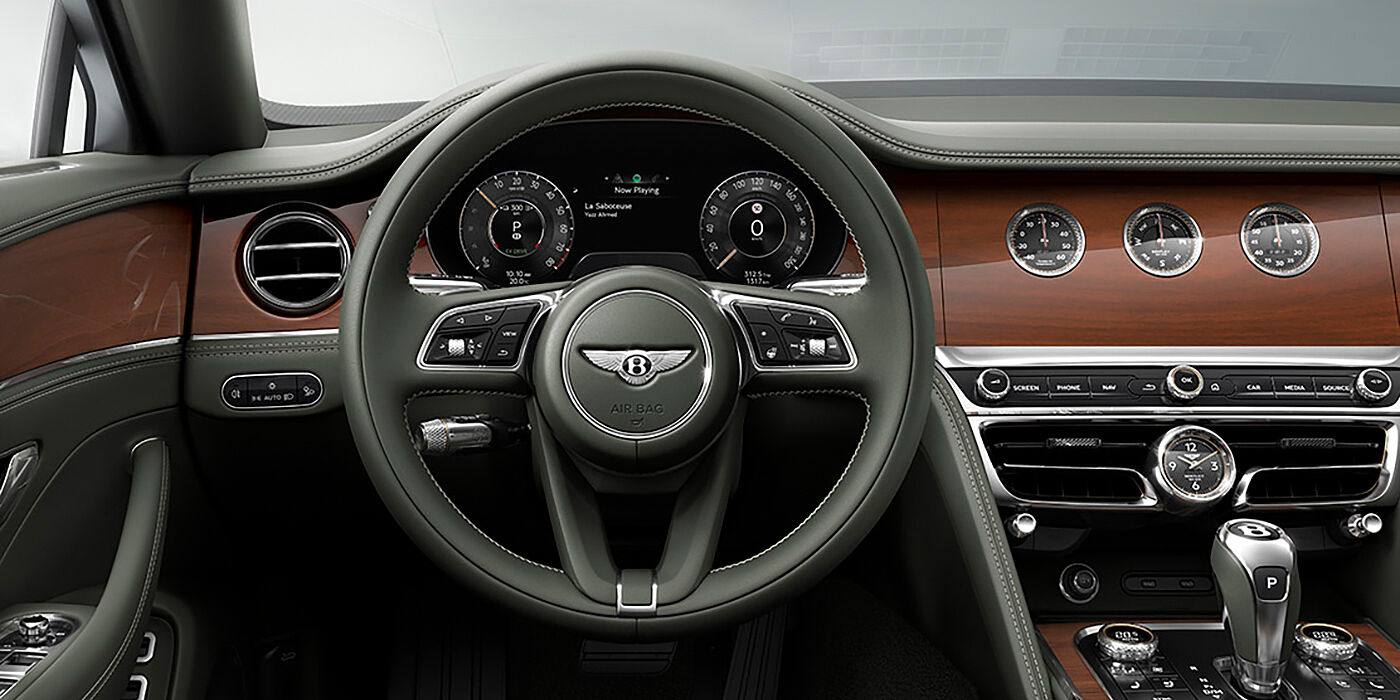 JCT600 Limited New Bentley Flying Spur sedan front cabin in Cumbrian Green hide and Crown Cut walnut veneer showing steering wheel and Rotating Display with three clocks on face
