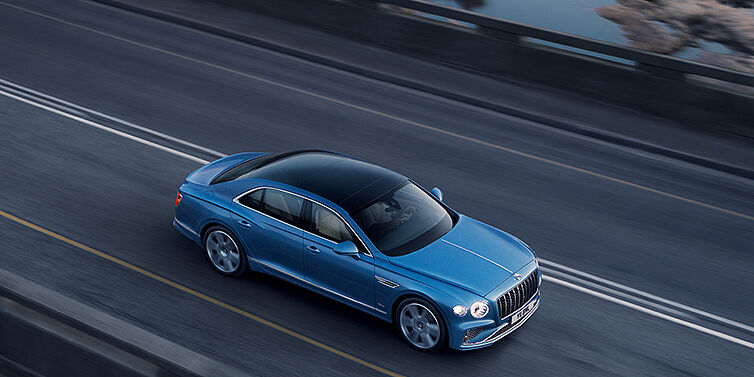 JCT600 Limited New Bentley Flying Spur Azure sedan in Light windsor blue paint by Mulliner, with 22 inch Azure wheels seen from overhead driving dynamically on a country road