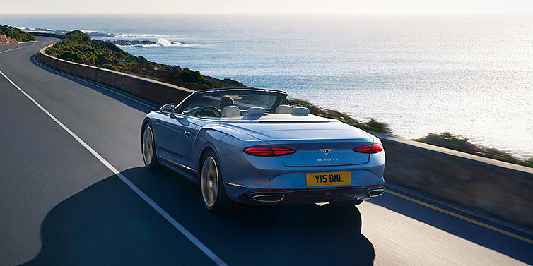 JCT600 Limited New Bentley Continental GTC Azure convertible rear view in Light Windsor blue paint with 22 inch ten spoke wheels driving dynamically on an ocean road in the sunshine